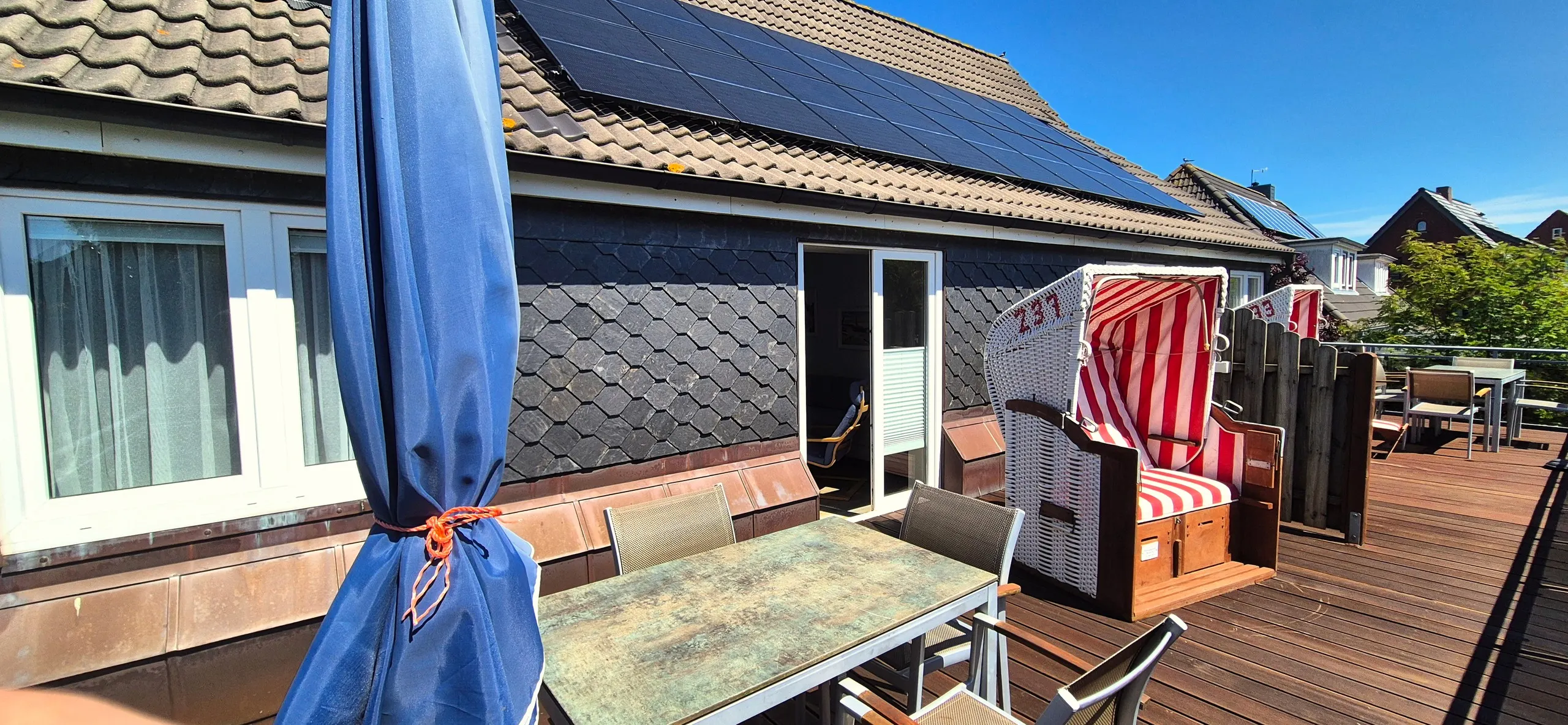 Regenpfeifer – Großzügige Dachterrasse mit Holzdielenboden, Sitzgruppe aus Metalltisch mit Glasplatte und mehreren Stühlen sowie einem …