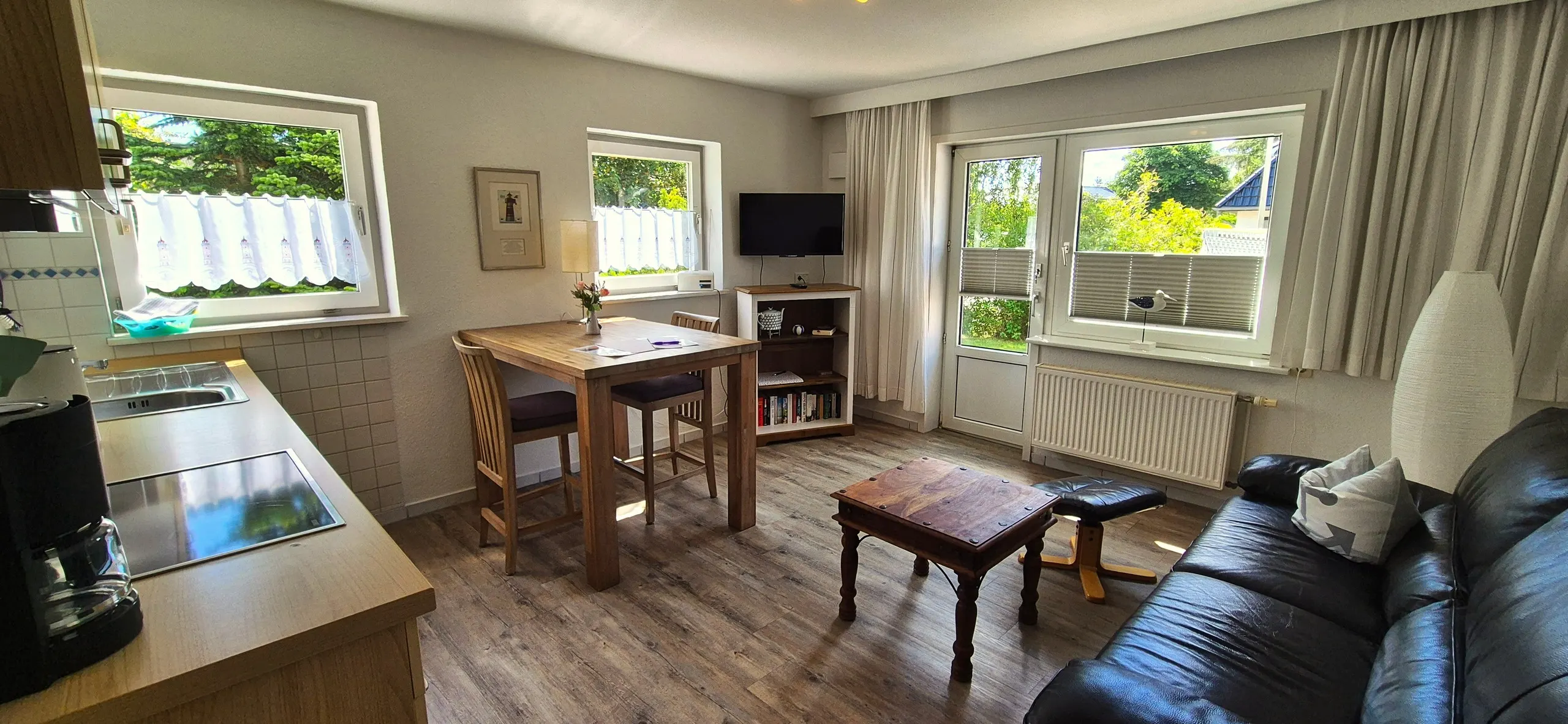 Krabbe – Offener Wohnbereich mit Esstisch für zwei, Fernseher auf Sideboard, Ledersofa und Terrassentür zum Garten.