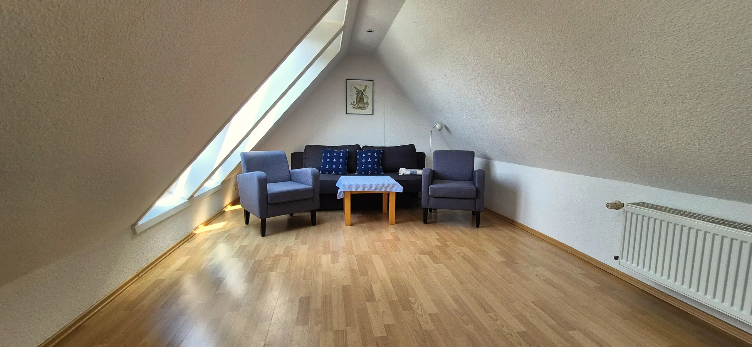 Glockenblume – Wohnzimmer im Dachgeschoss mit dunkelgrauem Sofa, zwei maritimen Anker-Kissen und zwei flankierenden grau-blauen …