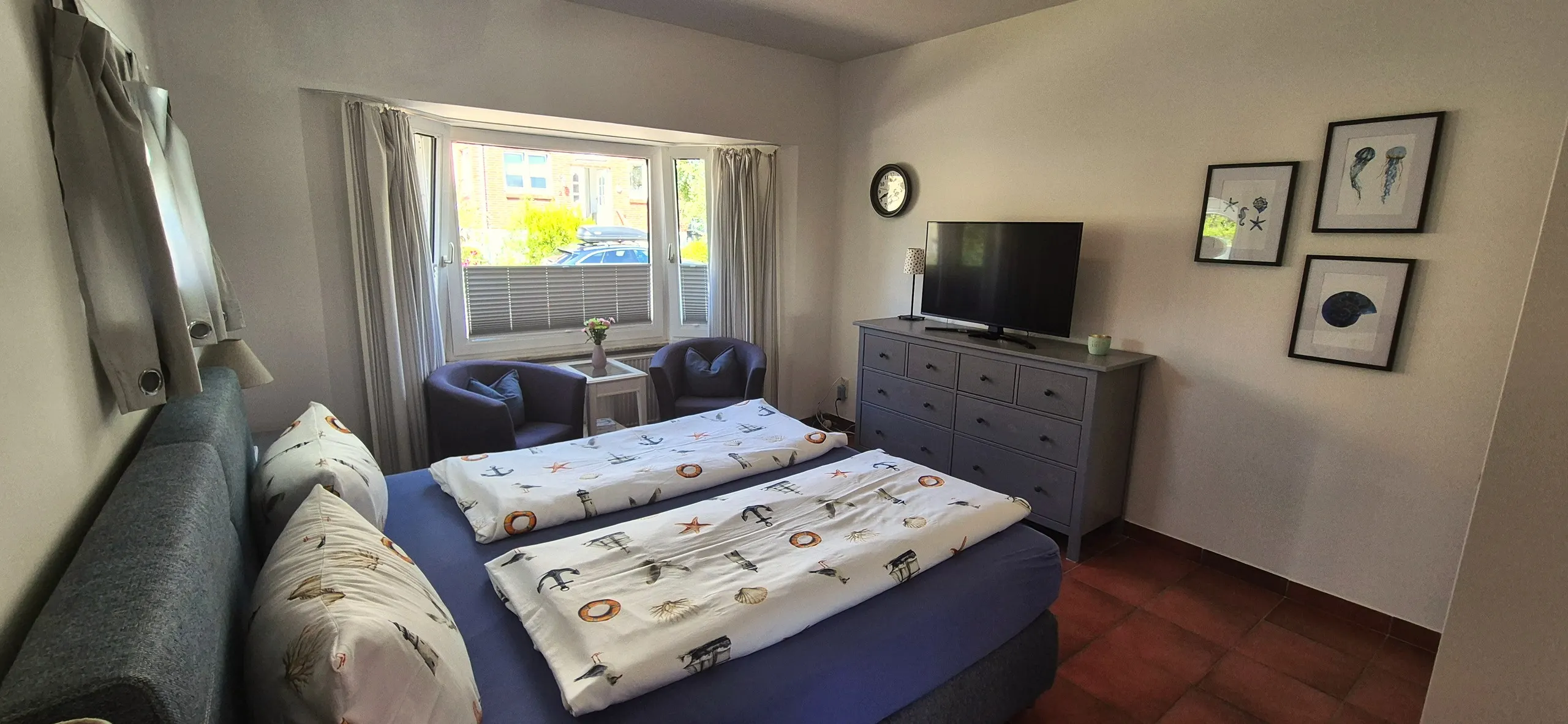 Tanzmaus – Schlafzimmer mit Doppelbett im Vordergrund, davor eine Sitzecke mit zwei blauen Sesseln und Beistelltisch vor einem …