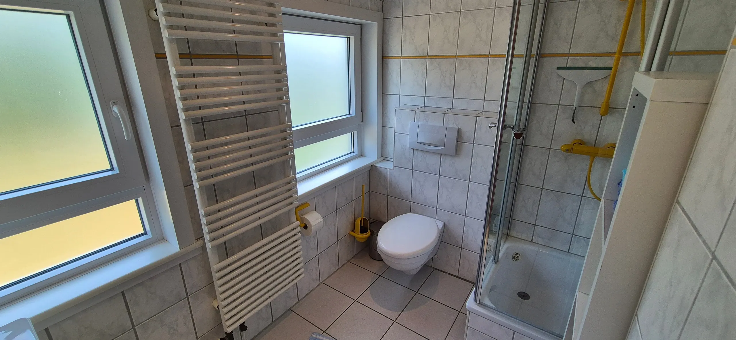 Dünenrose – Modernes Badezimmer mit hellgrauem Fliesenspiegel und gelbem Zierstreifen.