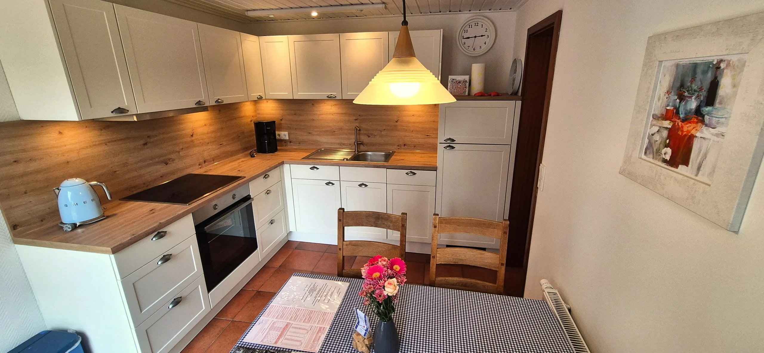 Spitzmaus – Offene Landhausküche mit weißen Fronten, Holzarbeitsplatte, Kaffeemaschine und Kühlschrank.