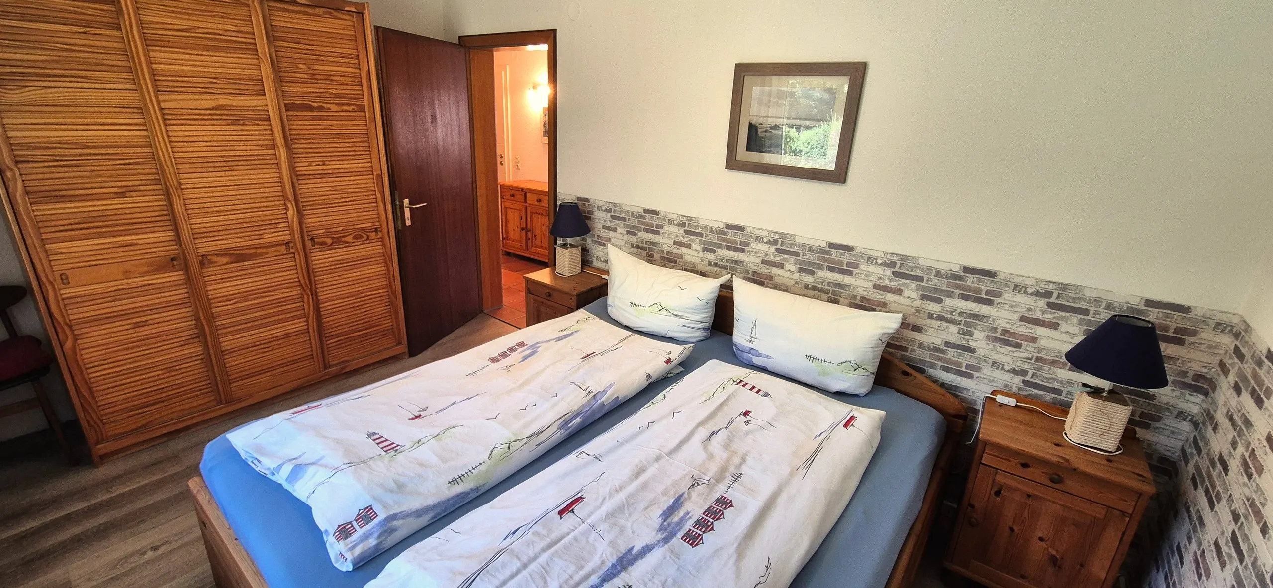 Butt – Schlafzimmer mit Doppelbett, Bettwäsche mit Leuchtturm-Motiv, großem Kleiderschrank aus Holz und zwei Nachttischen mit …