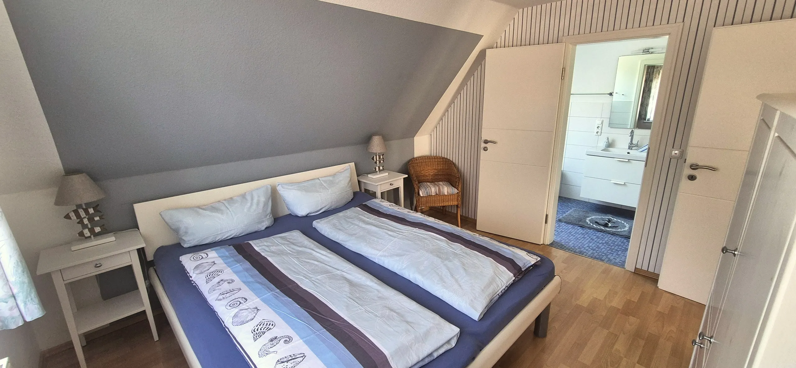 Seestern – Schlafzimmer unter der Dachschräge mit grau gestrichener Schrägwand und gestreifter Holztapete.