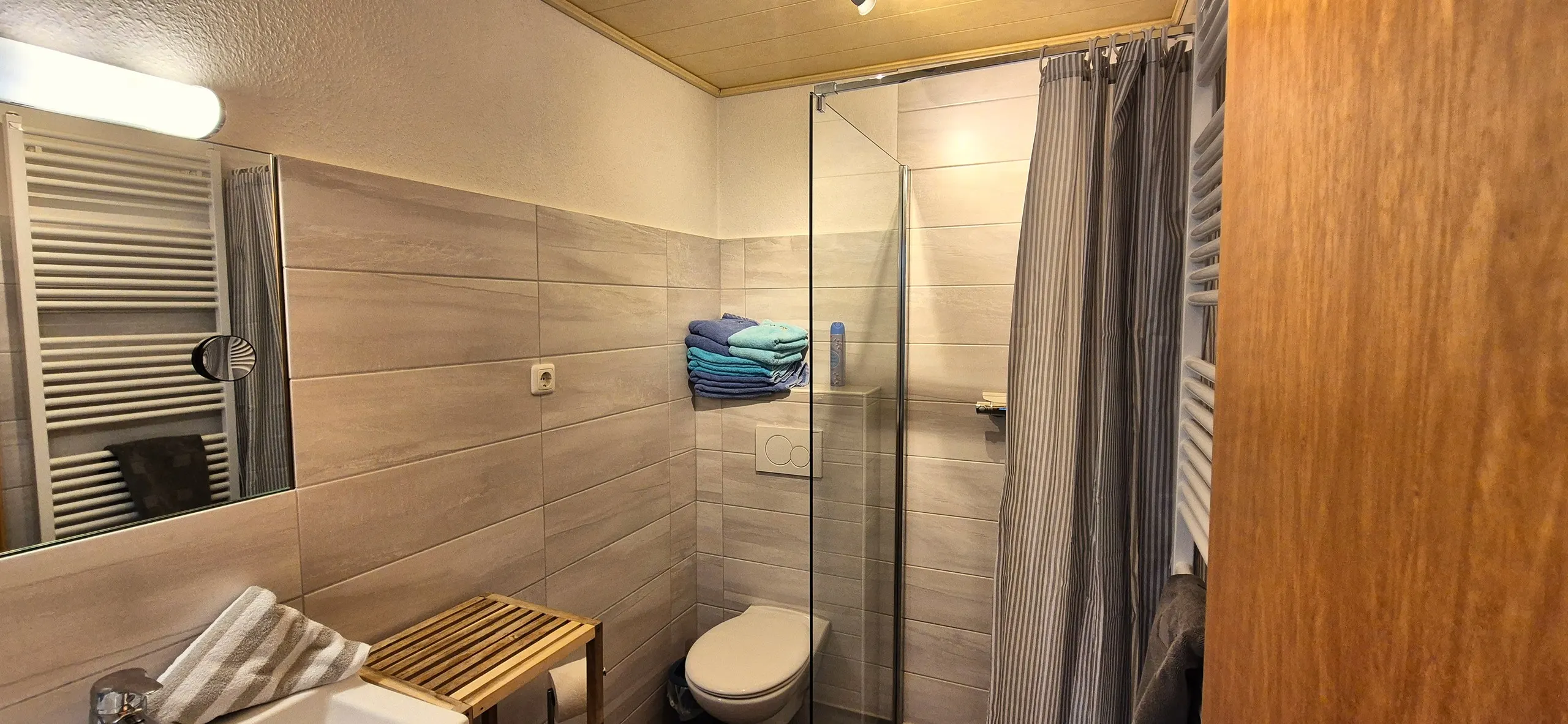 Grasnelke – Helles, modern gefliestes Badezimmer mit begehbarer Duschkabine mit Glaswand und gestreiftem Duschvorhang.