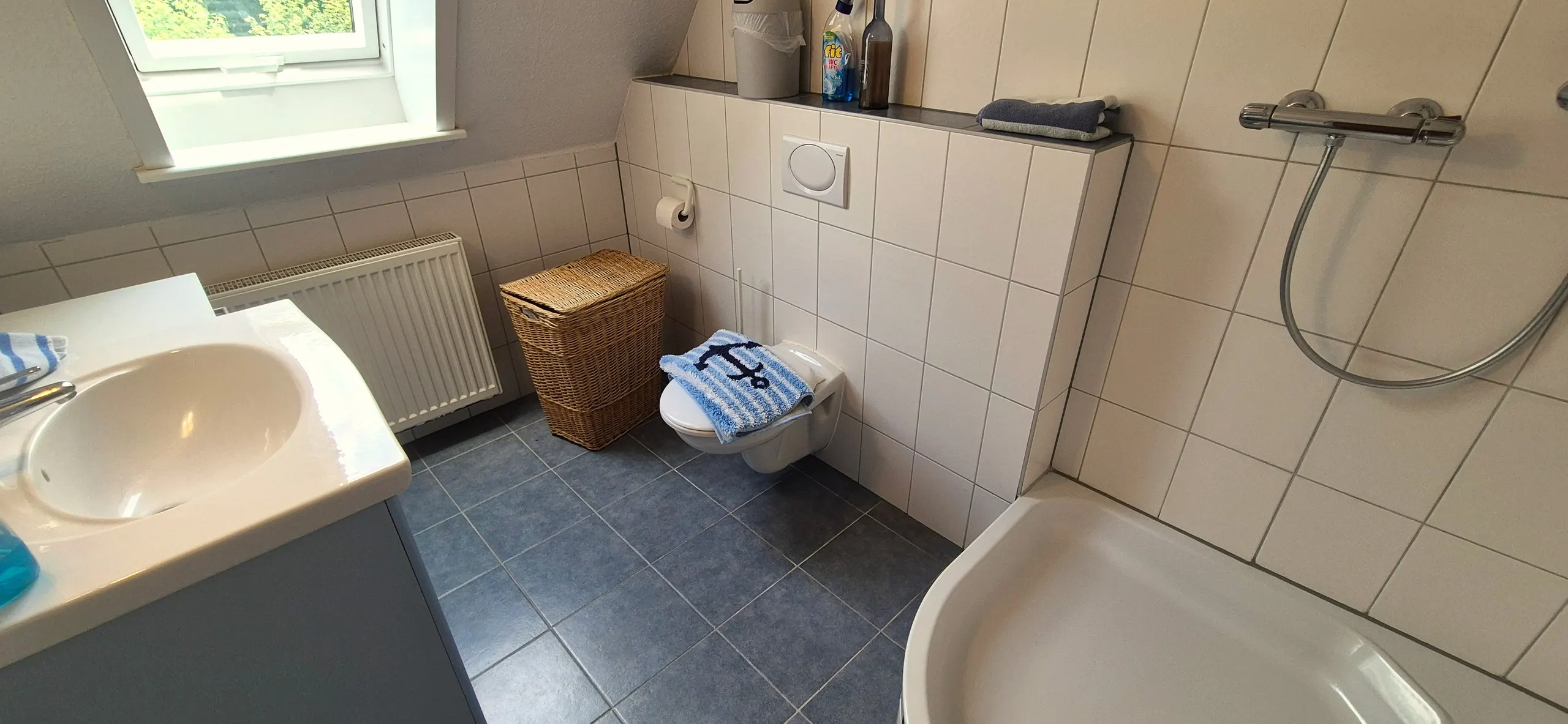 Blauer Salon – Badezimmer mit blaugrauen Bodenfliesen und weiß gefliesten Wänden, im Vordergrund eine Badewanne mit …