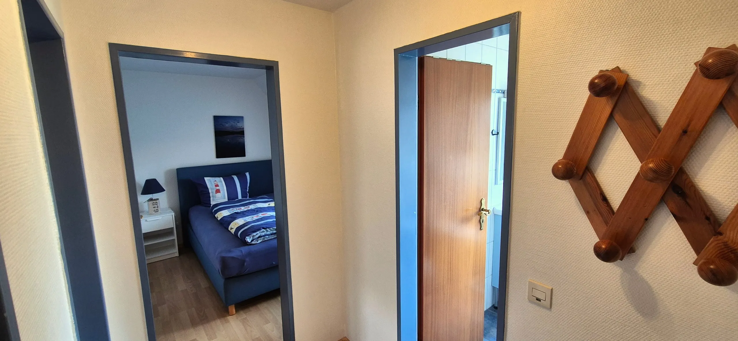 Glockenblume – Zentraler Flurbereich mit zwei offenen Türen: links ein Blick ins blau gehaltene Schlafzimmer mit Bett und weißem …