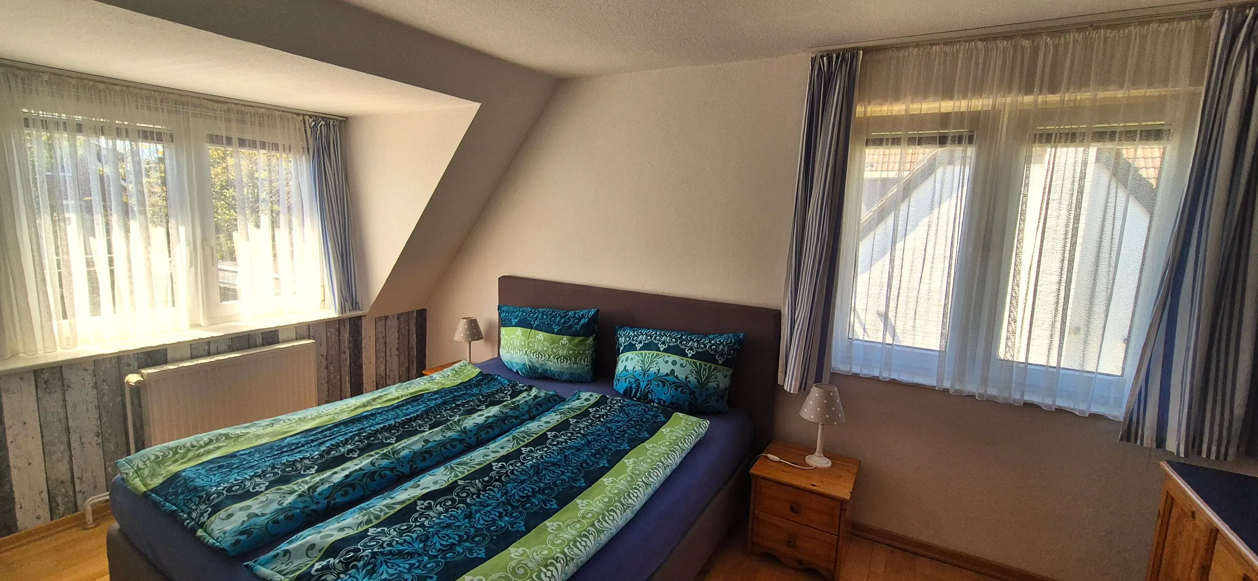 Regenpfeifer – Helles Schlafzimmer unter einer ausgeprägten Dachschräge mit Doppelbett, bezogen mit einer türkis-grünen, ornamental …
