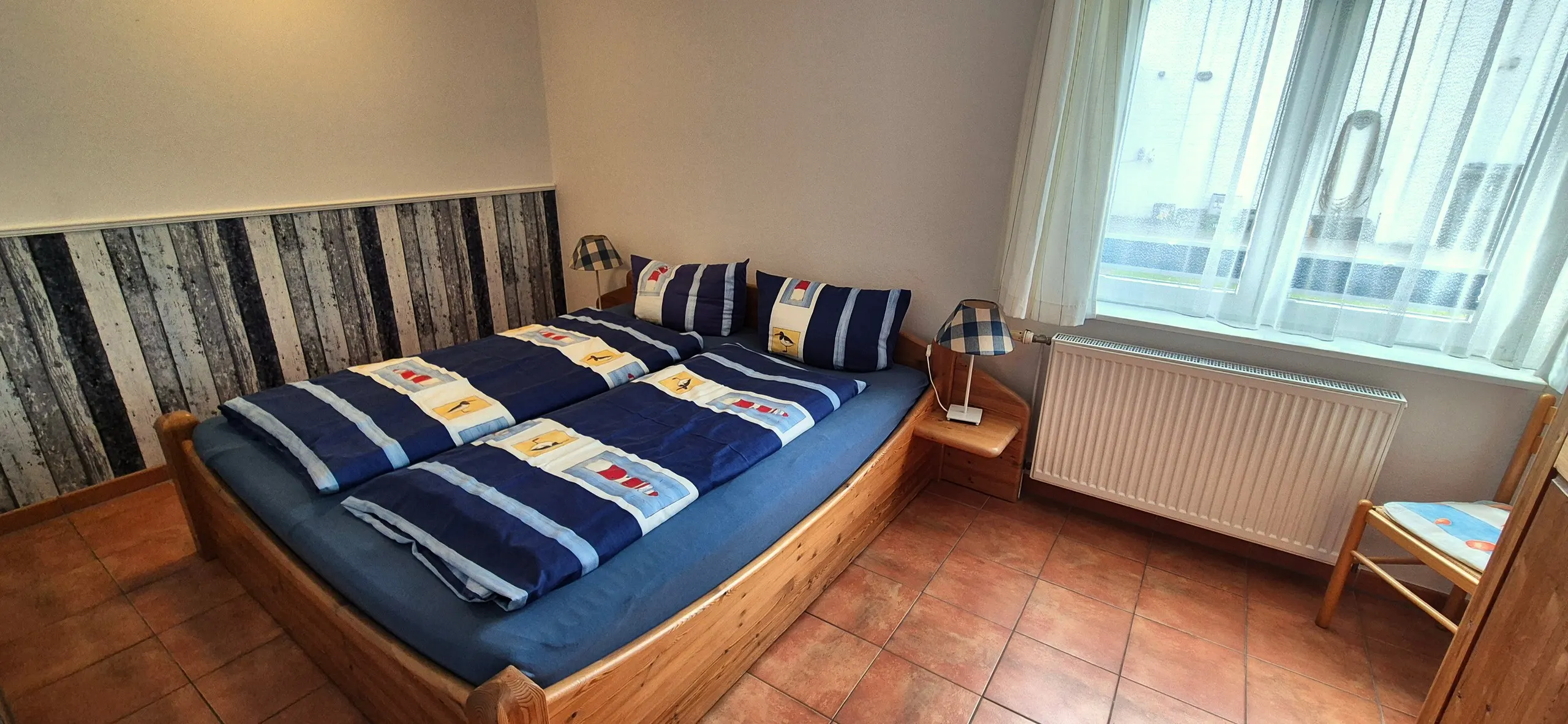Austernfischer – Zweites Schlafzimmer mit hellem Holzbett und marineblau-weiß gestreifter Bettwäsche mit Strandkorb-Motiven, dahinter …