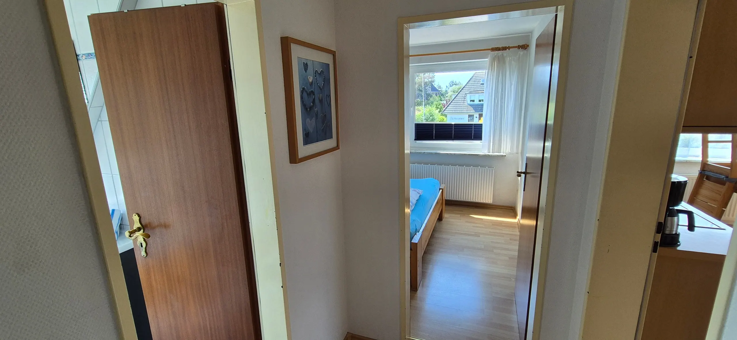Wollgras – Flurbereich mit brauner Zimmertür links und gerahmtem Bild mit Herzmotiven an der Wand, geradeaus öffnet sich der Blick …