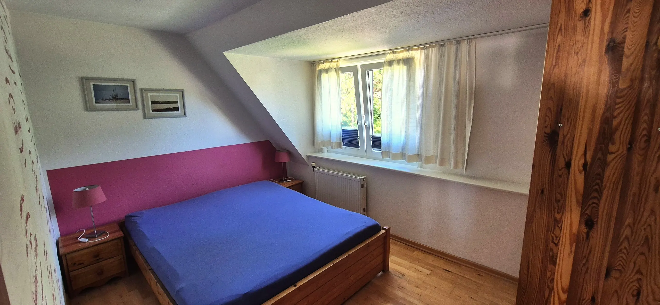 Regenpfeifer – Schlafzimmer mit Doppelbett und kräftig blauer Bettwäsche vor einer pink-magentafarbenen Akzentwand, die bis zum …