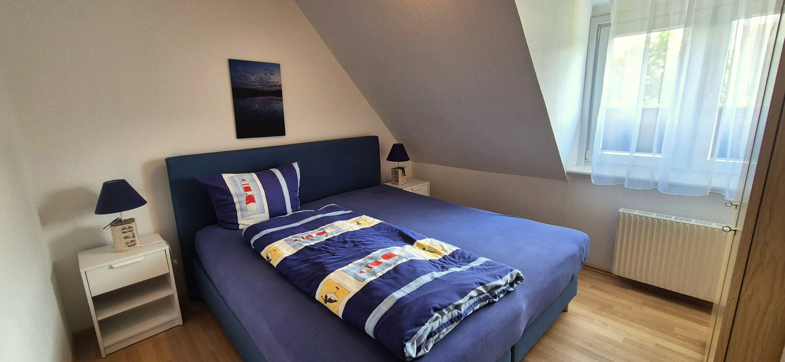 Glockenblume – Schlafzimmer unter Dachschräge mit Doppelbett, dunkelblauem Bettbezug und einer Bettdecke mit maritimem Muster …