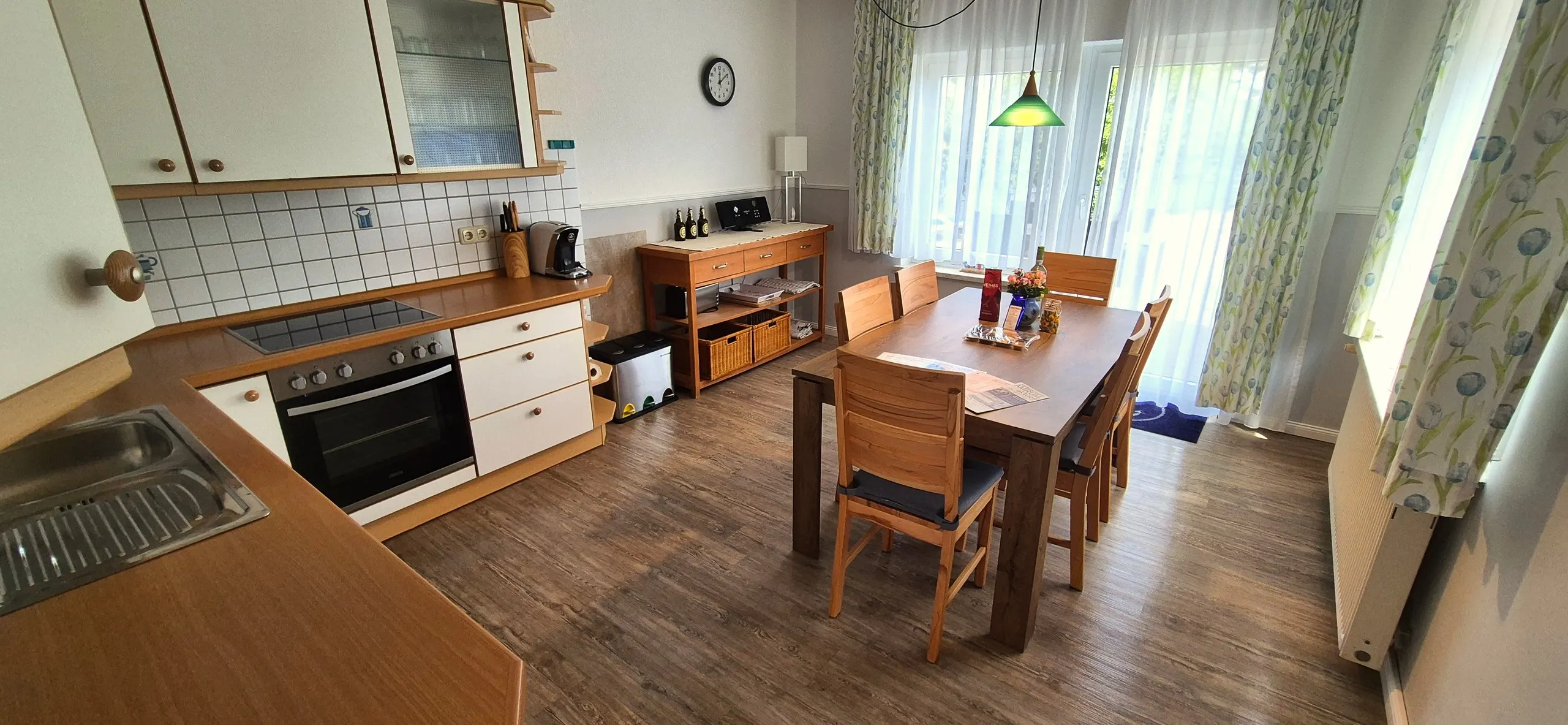 Küstenhaus – Offener Wohn-Essbereich mit L-förmiger heller Einbauküche, Ceranfeld, Backofen und weißen Oberschränken mit …
